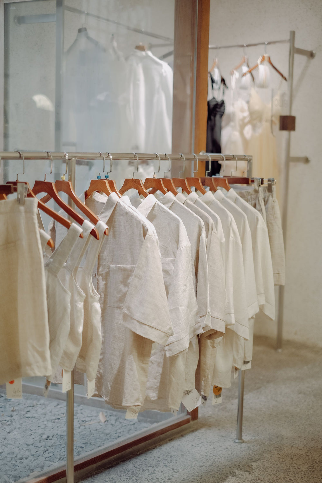 Minimalist clothing boutique featuring white garments on wooden hangers, a metal clothing rack, and soft neutral interiors.